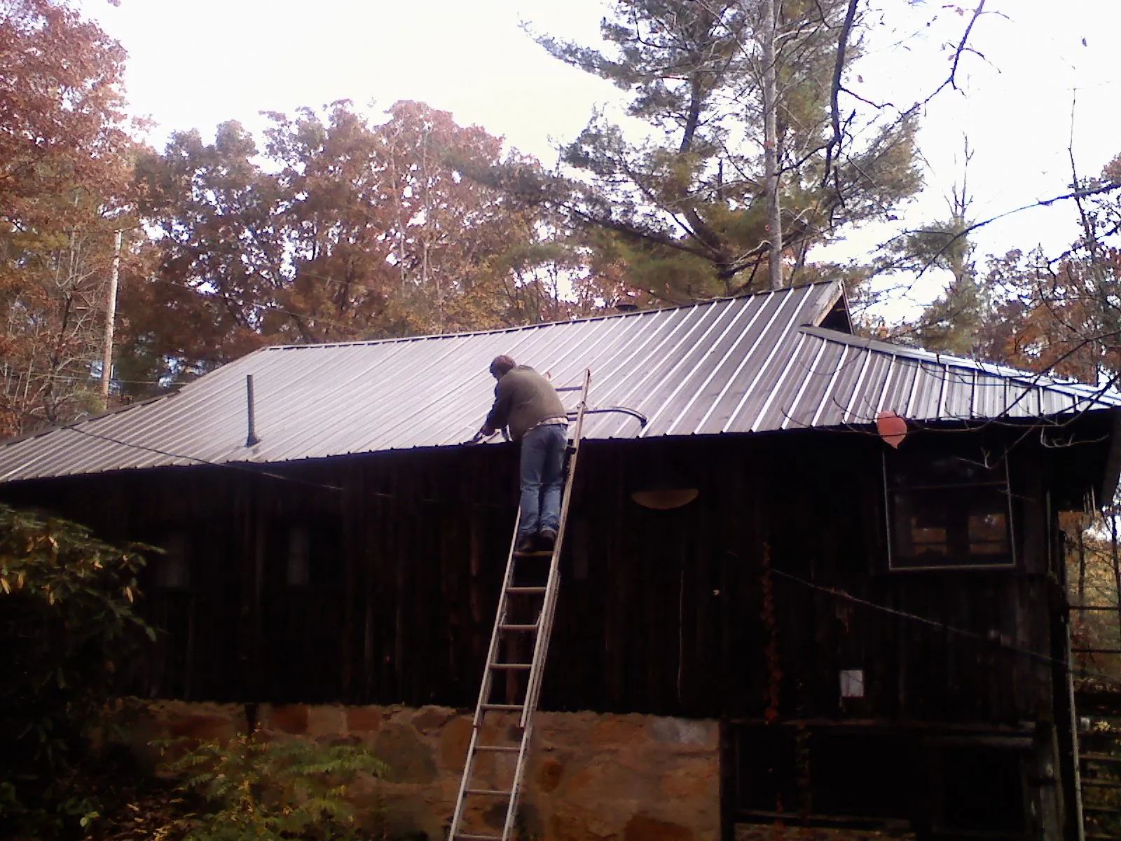 Roofer on a ladder working along the edge of a cabin metal roof in Auburn