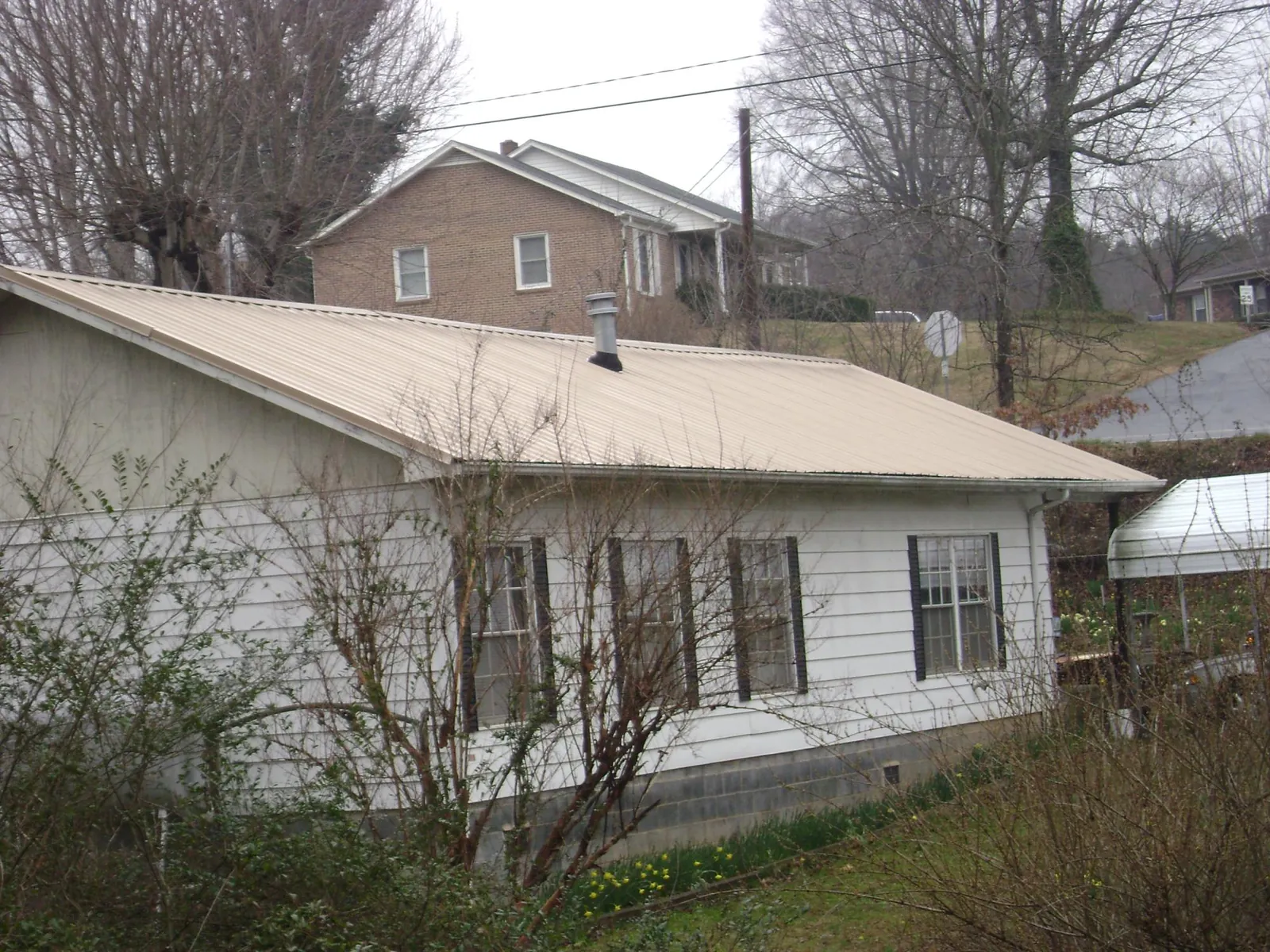 Tan metal roof on a white sided house set into a hillside — Commercial Roofing by Roofing Brothers in Auburn